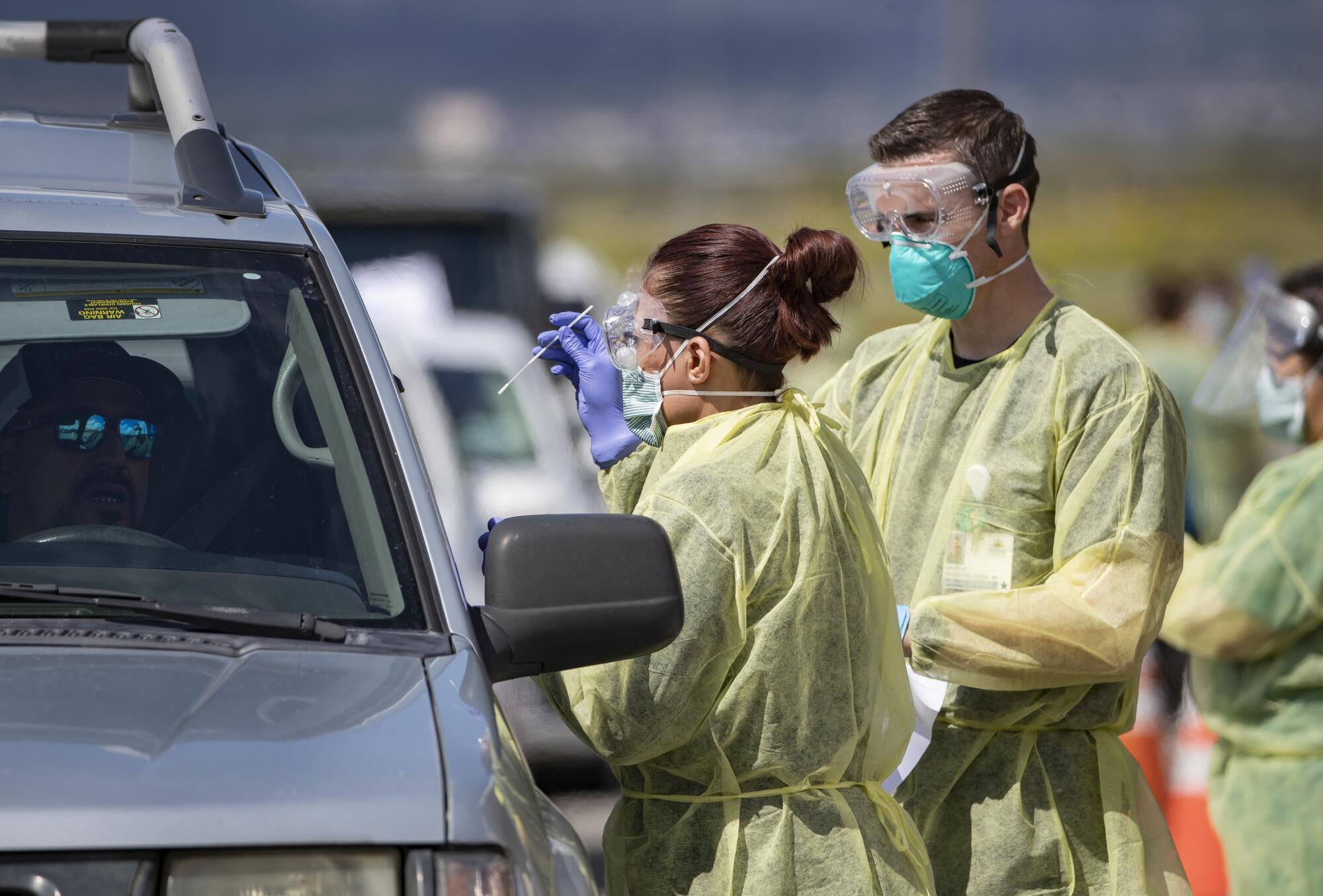 Riverside County medical personnel administer a coronavirus test to a driver at a drive-though testing facility at Diamond Stadium.