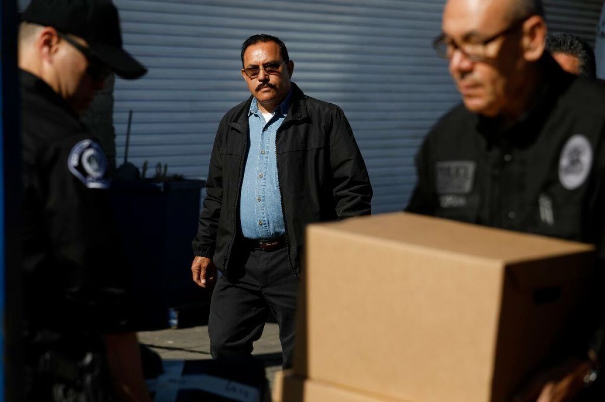 Then-Mayor Ramon Medina keeps an eye on investigators from the L.A. County district attorney's office while they remove computers and other material from his auto repair shop.