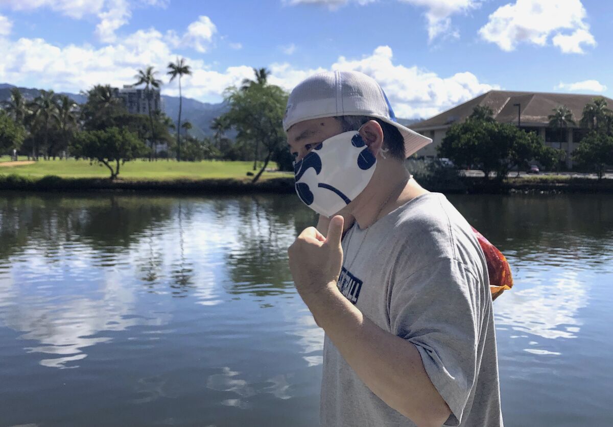 Ricardo Lay wears an aloha-print mask and flashes a shaka sign as he walks in the Waikiki neighborhood of Honolulu.
