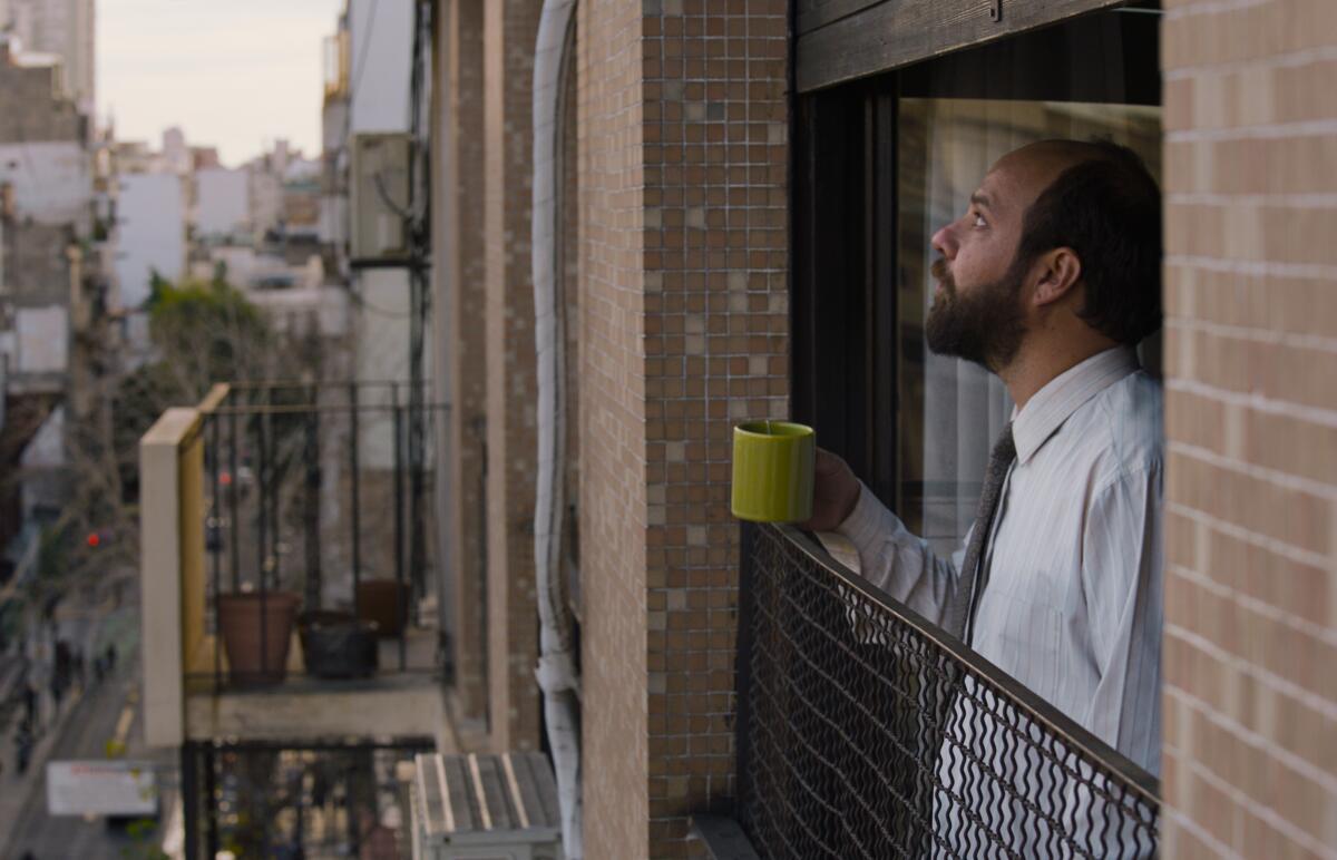 A man holds a mug and stares out his window.