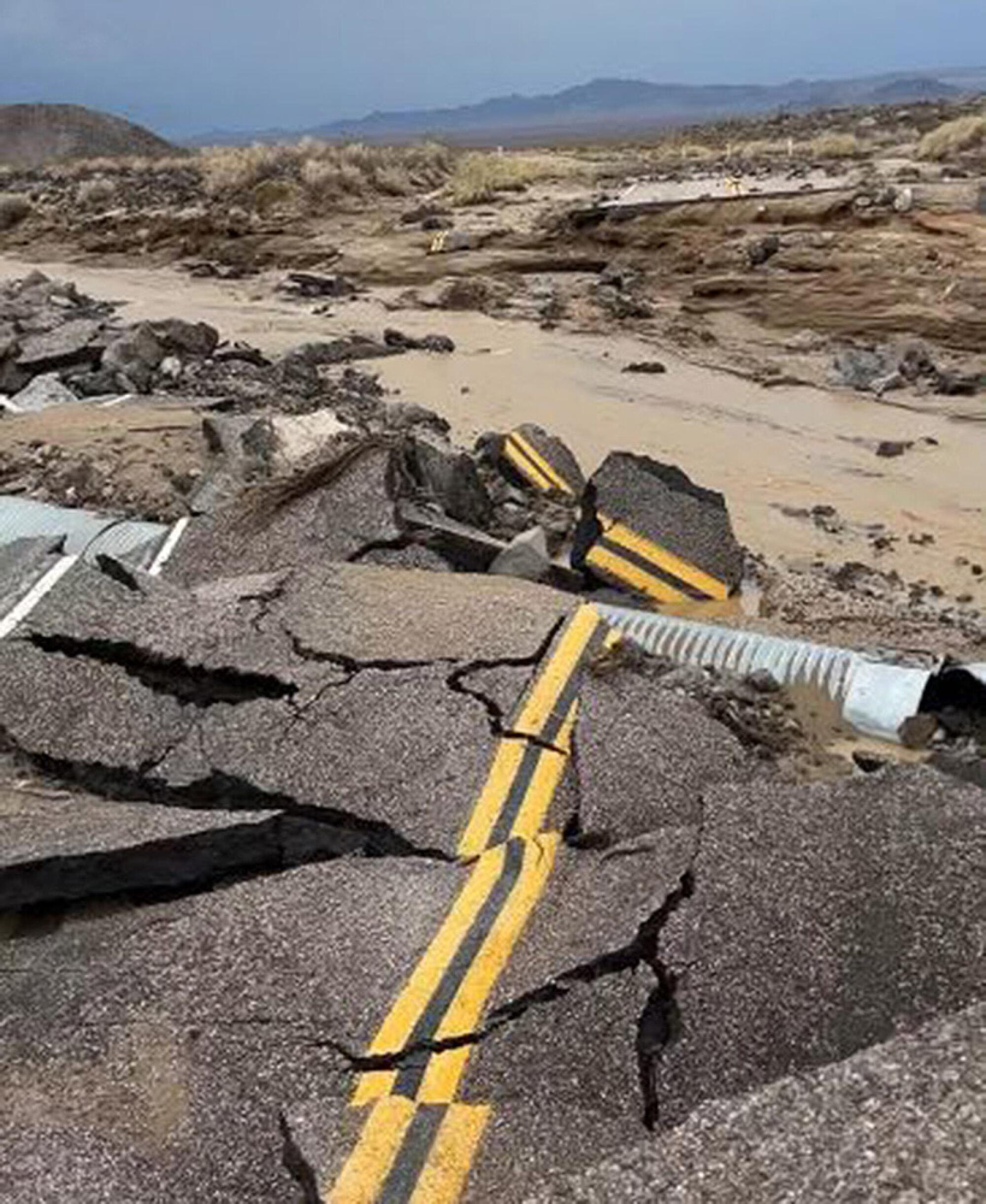 A broken and warped road is surrounded by mud.