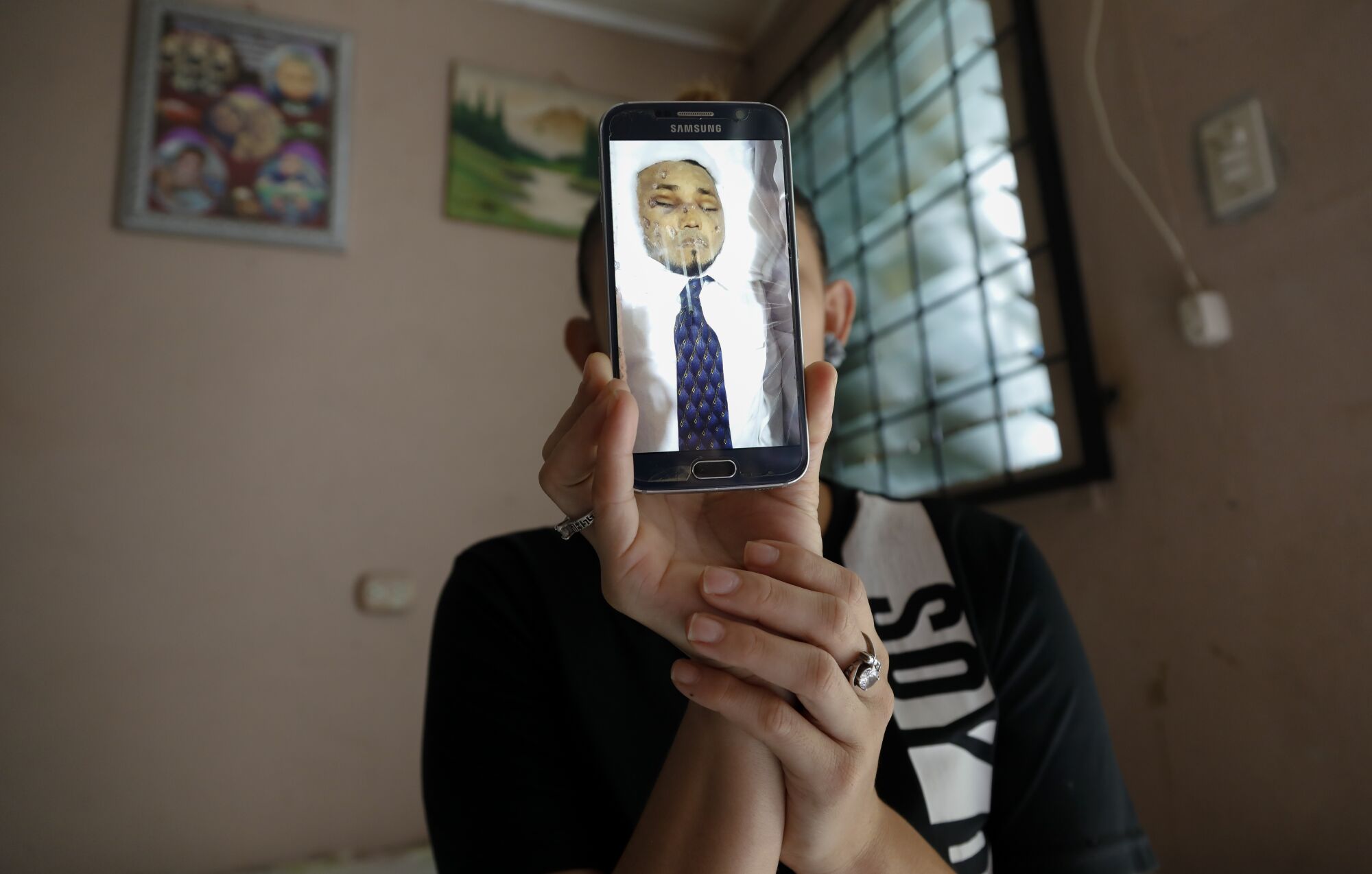 Nilsa Rosibel Estrada Villanueva holds up a digital photo of her brother, Yovin Estrada Villanueva, in his casket.