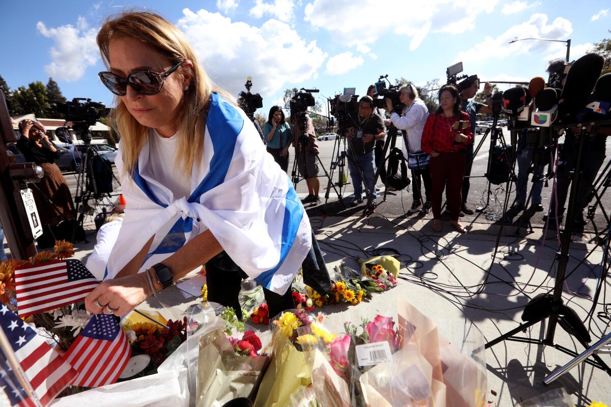 Anat Joseph, draped in an Israel flag, leaves American flags at a growing memorial for Paul Kessler.