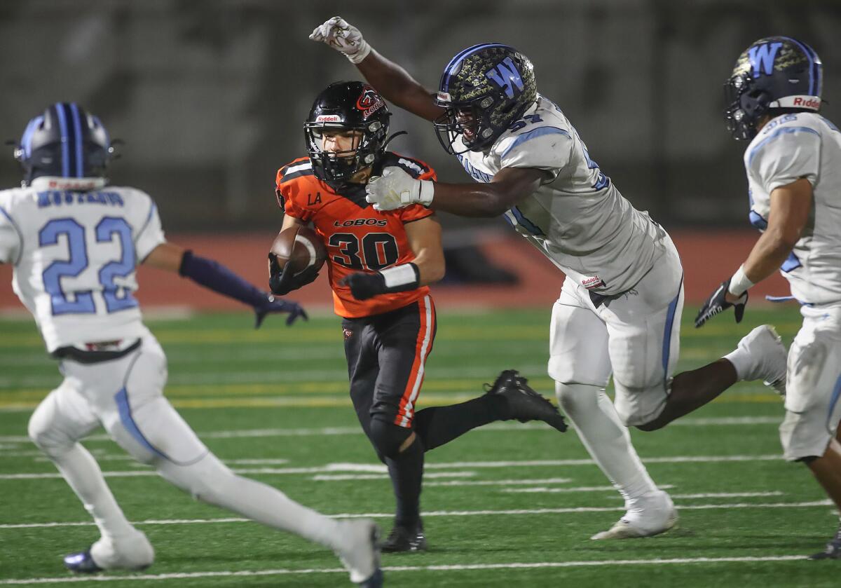 Los Amigos' Isaac Galindo (30) runs to escape the grasp of Walnut's Demaja Windom as he looks for a first down on Friday.