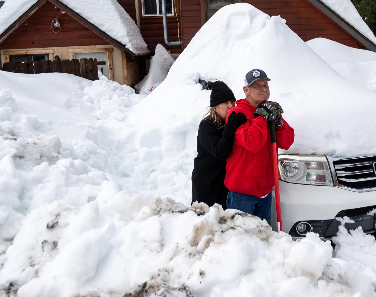 A woman leans on a man holding a shovel as the two are surrounded by snow.