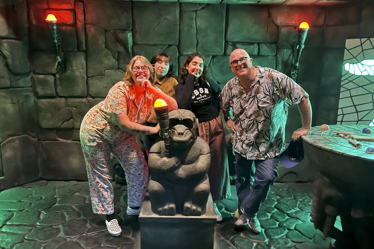 Four people clustered around a monkey statue in a Jumanji-themed escape room.
