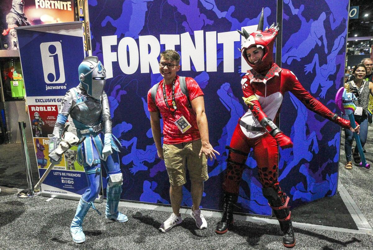 Three people dance in front of a sign reading "Fortnite."
