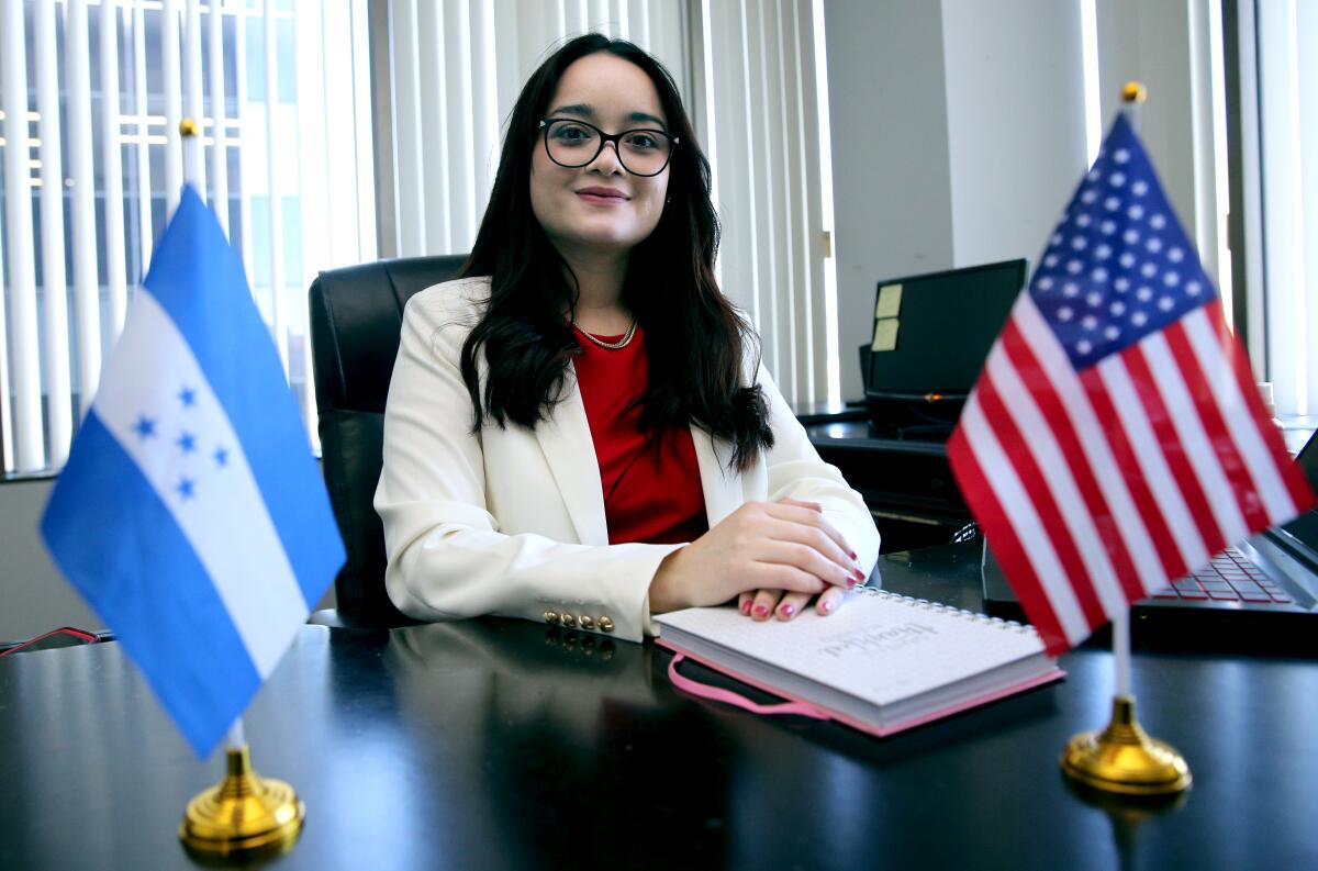 A woman sits at a desk with two small flags on it.