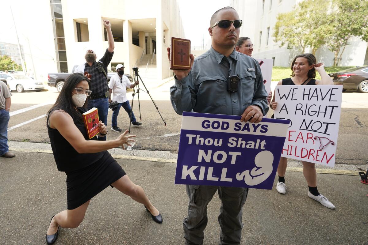 Anti-abortion activist Gabriel Olivier, center, holds his Bible and a message sign while abortion rights supporters hold counter signs and dance around him, as he and other anti-abortion supporters call out to people leaving the Hinds County Chancery Court, Tuesday, July 5, 2022, in Jackson, Miss., after a hearing in a lawsuit brought by the state's only abortion clinic that seeks to block a law that would ban most abortions. (AP Photo/Rogelio V. Solis)