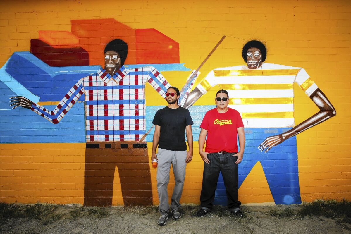 Coachella artists Armando Lerma, left, and Carlos Ramirez, known by the artist name the Date Farmers, have begun the Coachella Walls project, a mural project around their hometown, about three hours south of L.A., and are photographed with their piece "Casa de Trabajador."