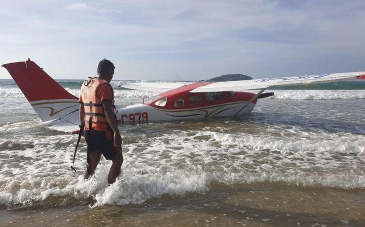 In this handout photo provided by the Philippine Coast Guard District Palawan, a rescuer walks beside a Cessna 206 plane carrying two pilots and 25 boxes of live fish after it crash-landed Friday Dec. 10, 2021, on the shoreline near the resort town of El Nido in western Palawan province, Philippines, due to engine trouble, civil aviation officials said. Philippine coast guard personnel rescued the two pilots from the floating aircraft near the beach, where the private plane ditched after taking off from San Vicente town in Palawan on a domestic flight to Sangley airport in Cavite province south of Manila. (Philippine Coast Guard District Palawan via AP)