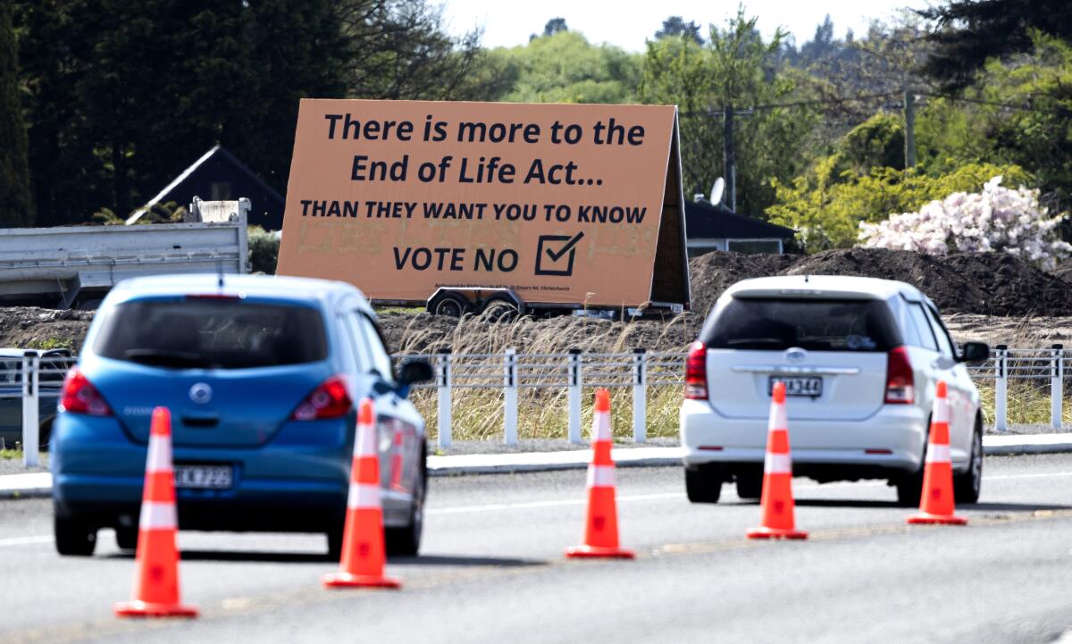 Cars driving by a billboard urging a no vote on a euthanasia law 