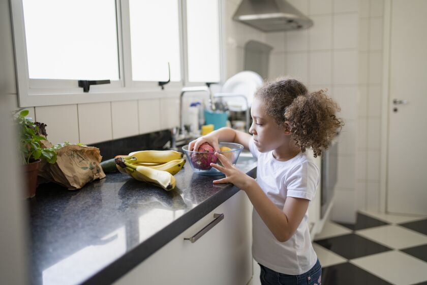 Little girl choosing fruit from a bowl on the kitchen counter at home.