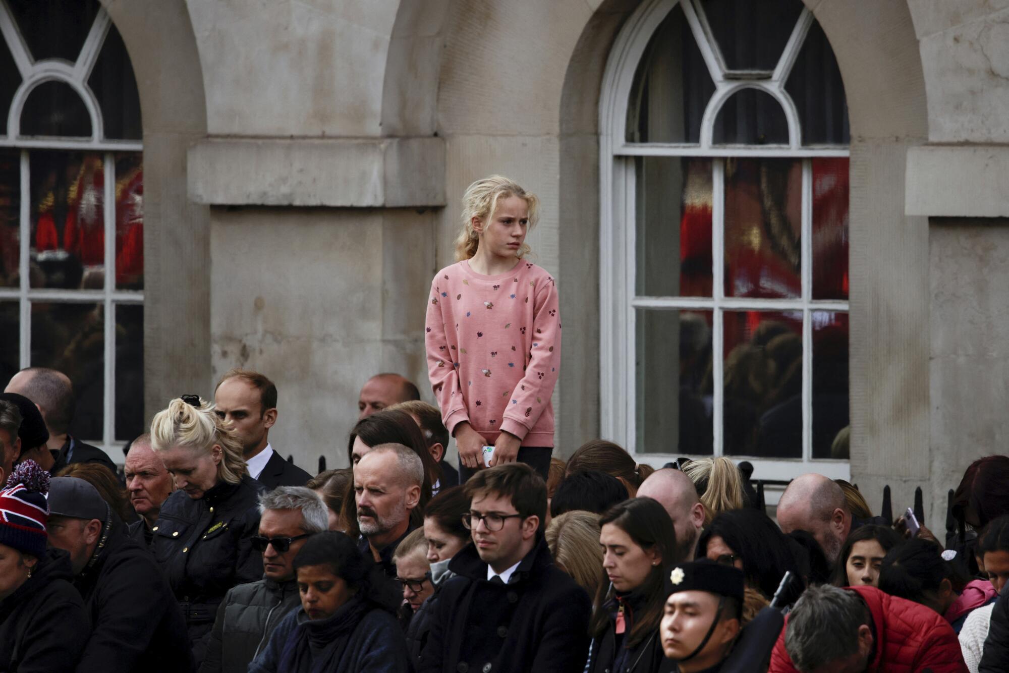A girl stands above an outdoor crowd and looks around during a period of silence.