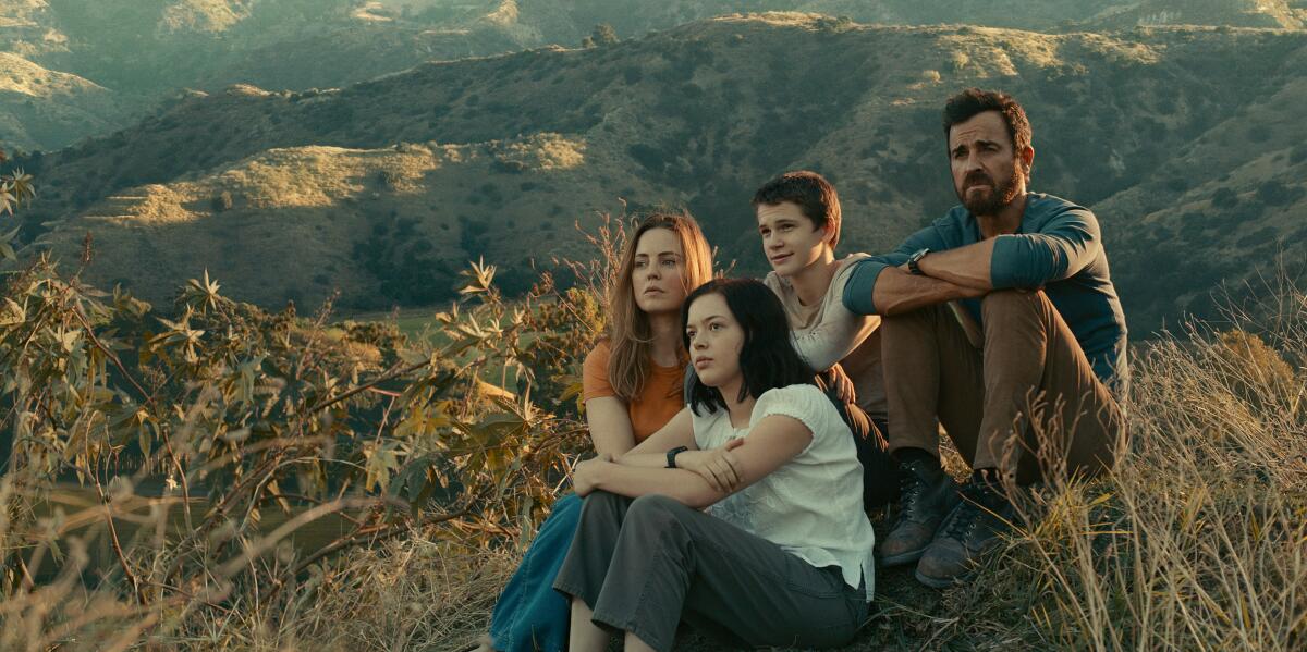 A family of four sits on a ridge in a remote mountain range