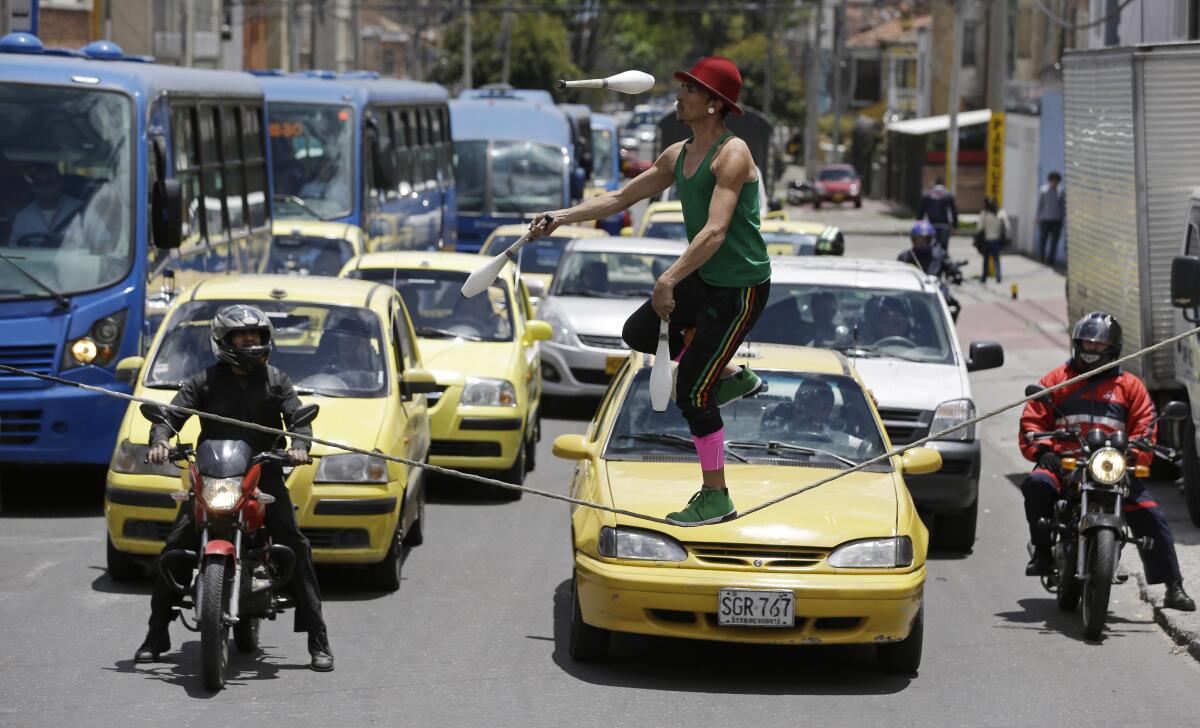 Taxis en espera en un semáforo mientras un malabarista callejero camina sobre una cuerda a cambio de propinas en Bogotá
