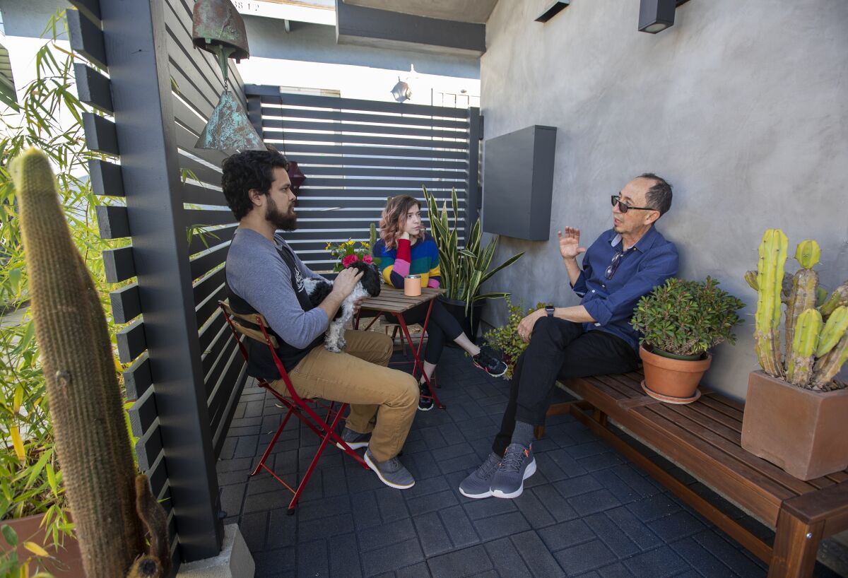Three people sit talking in an enclosed outdoor space with several cactuses nearby