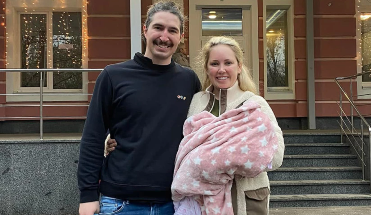 A man and woman with a baby in a blanket.