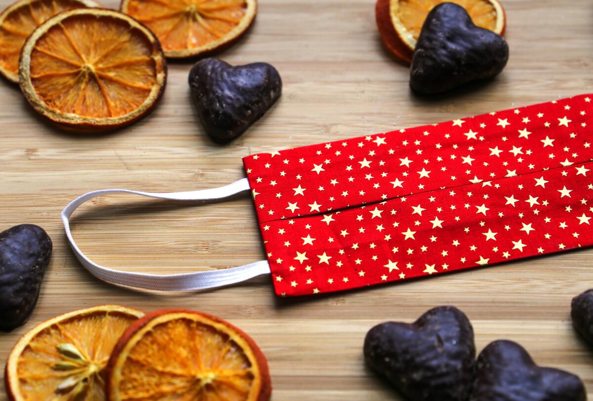 A holiday mask made from red cloth with gold stars sits on a table next to edible festive treats.
