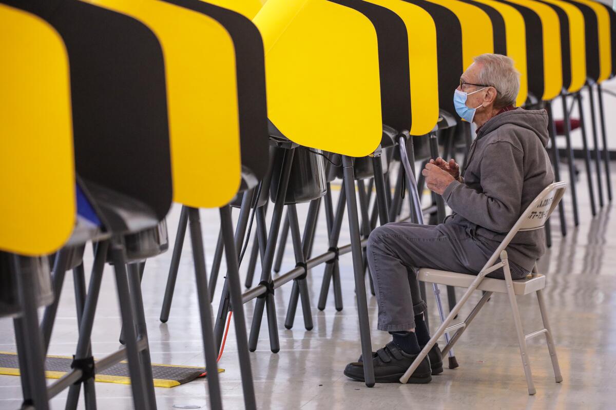 A seated man wearing a surgical mask casts his ballot.