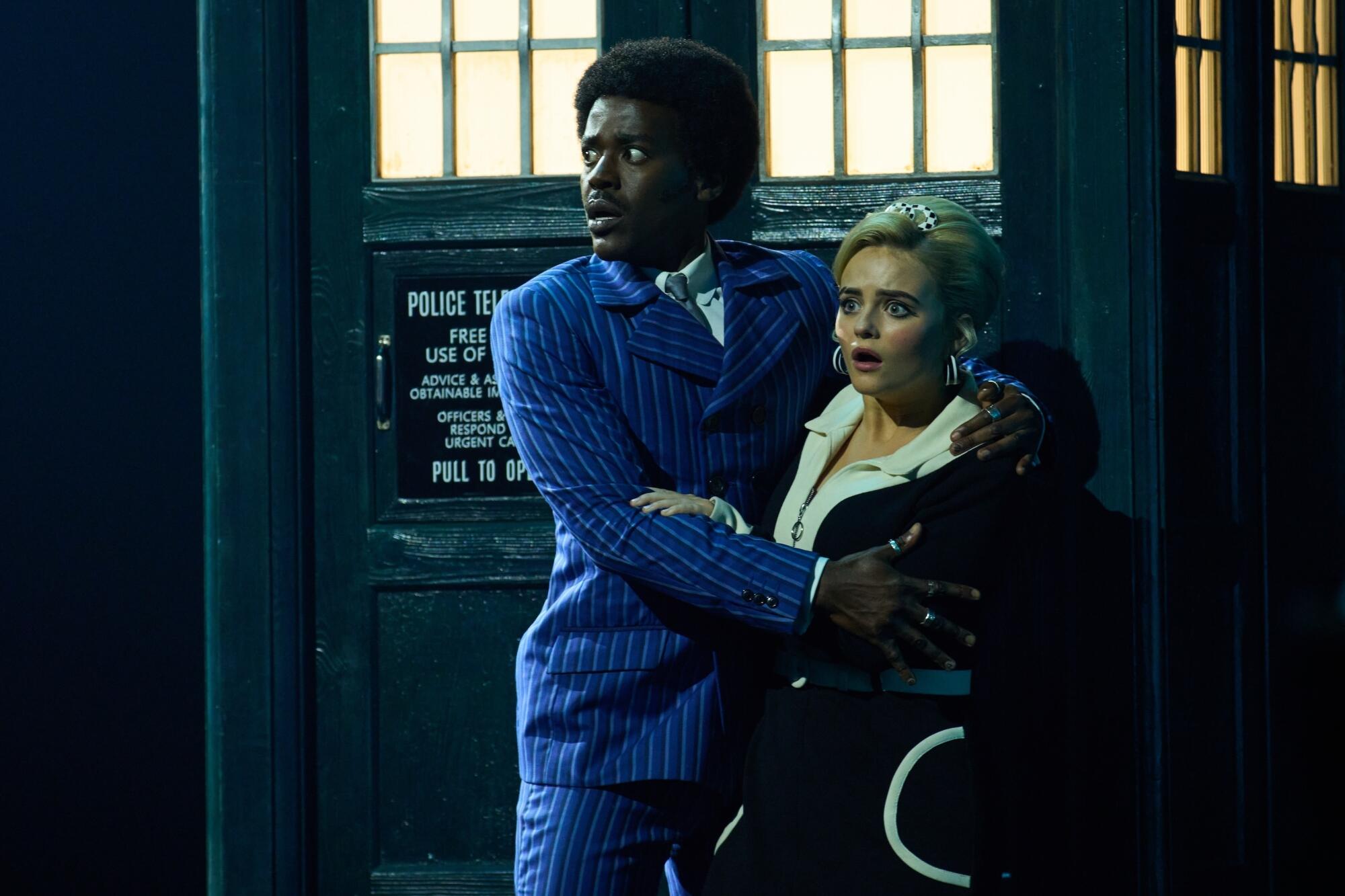 a man and a woman huddled together in front of a police box