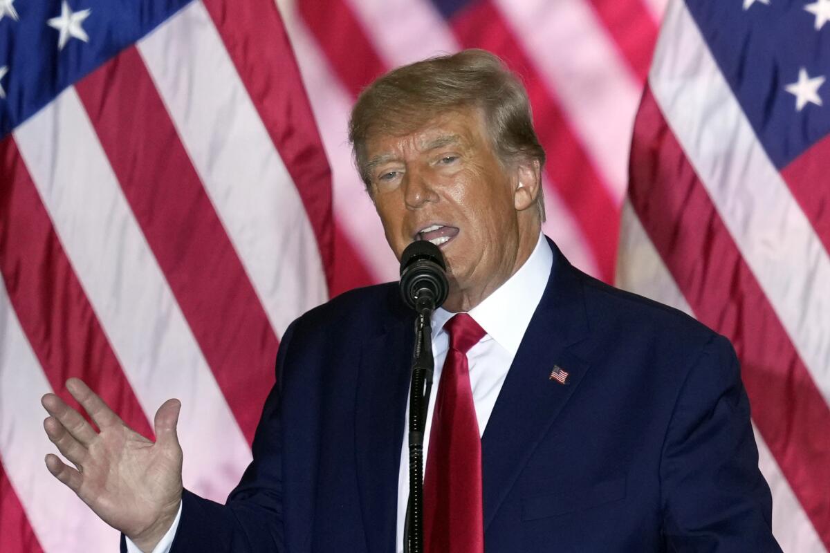 Former President Trump speaks in front of a flag.