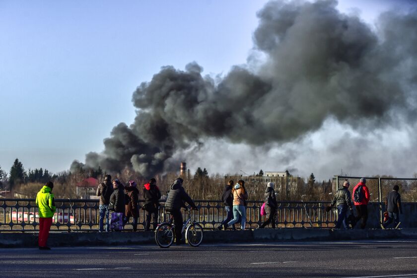 People walk as a cloud of smoke raises after an explosion near the airport, in Lviv, western Ukraine