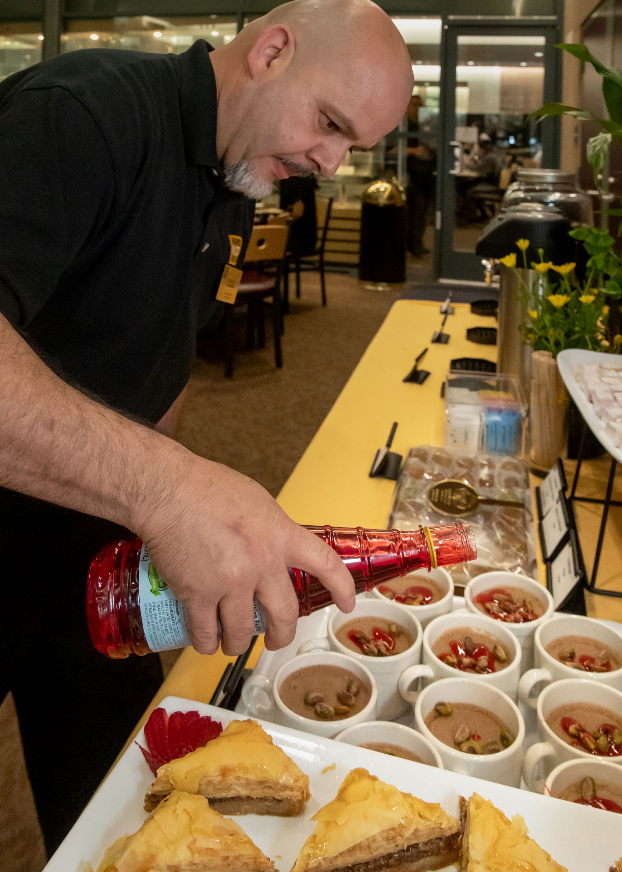 Miguel Ruvalcaba pours a red sauce over cups of brown pudding.