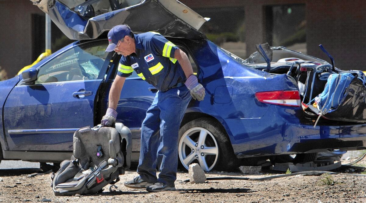 A tow truck operator picks up a child's seat at the scene of a two-vehicle accident in which five people were killed inside the blue Honda at the intersection of Main Street and Balsam Avenue in Hesperia.