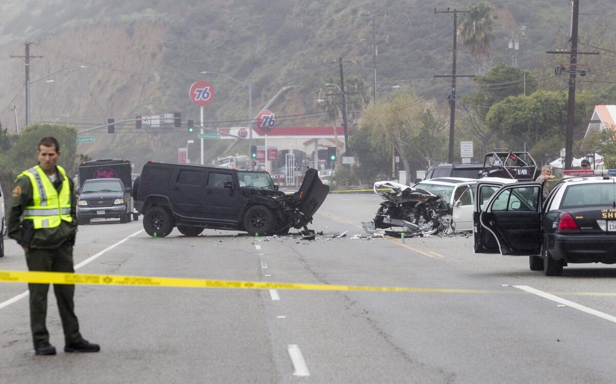 A Los Angeles County Sheriff's deputy guards the scene on Corral Canyon Road in Malibu. One person was killed and five were injured in the crash.