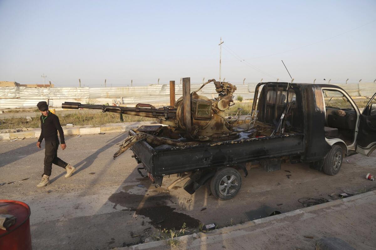 A member of an Iraqi Shiite militant group called Imam Ali Brigades strolls past a damaged vehicle in Tikrit on March 25.