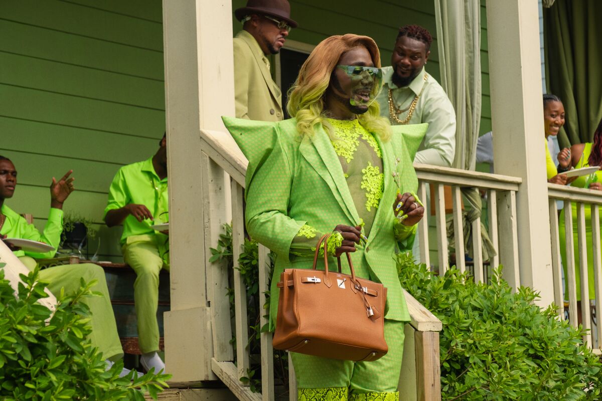 A man in a neon green suit descends the steps from the front porch of a house.