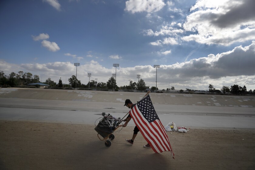 A homeless man carries the U.S. flag along the Santa Ana River channel.