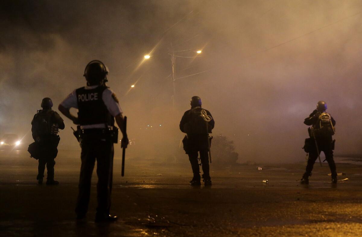 Law enforcement officers watch early Sunday as canisters are fired to disperse a Ferguson, Mo., crowd defying a midnight curfew to protest the fatal shooting of Michael Brown.