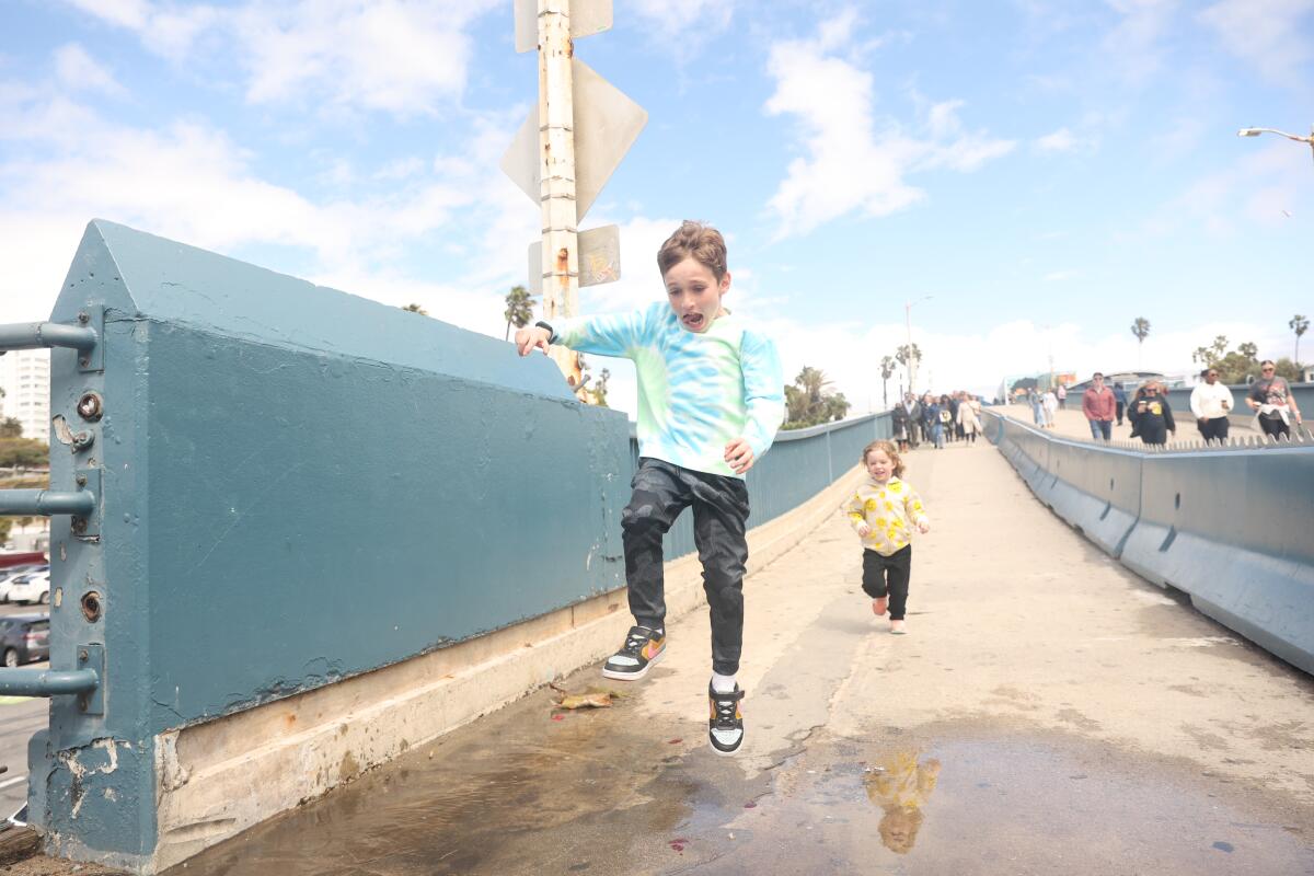 A boy jumps over a rain puddle as his sister runs behind him at Santa Monica Pier.