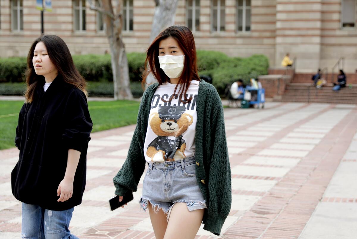 Two young women, one wearing a mask, walk in front of a building