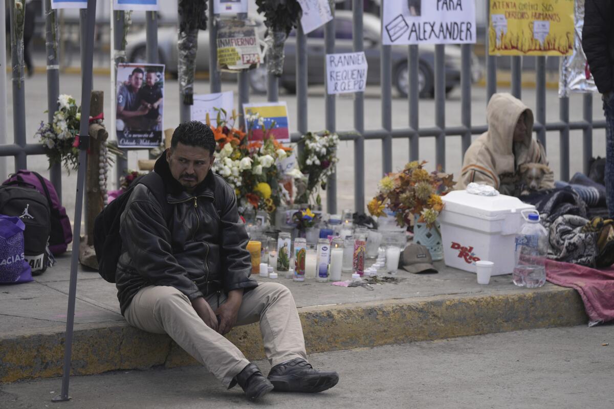 A man sits on the sidewalk near an altar of candles and photos.