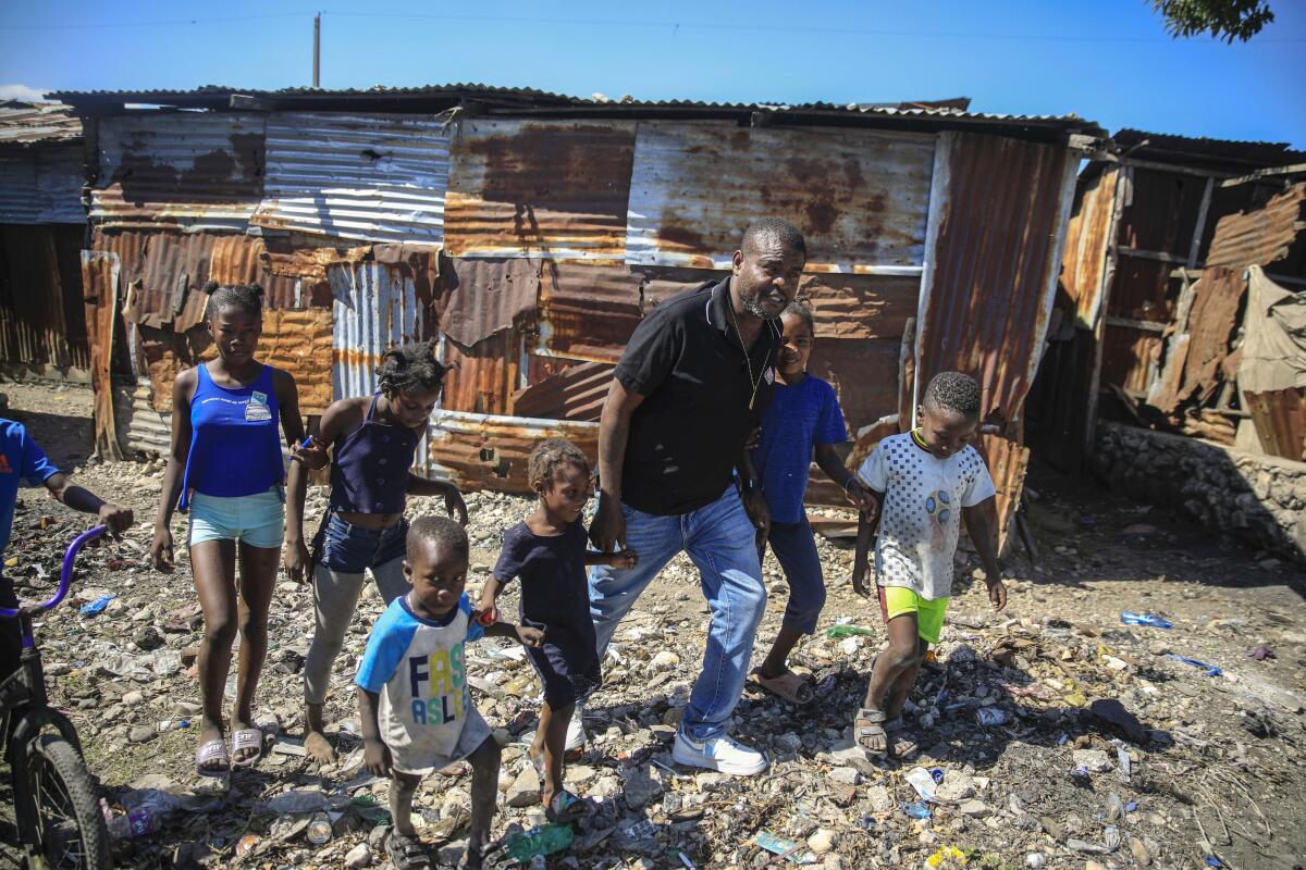 A man walks with children near a rusted metal shack 