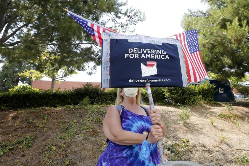 Valerie Honn, from the city of Orange and a 32-yr. postal carrier who recently retired, stayed holding a sign after A Save the USPS rally at the Camelback Street post office in Newport Beach, on Tuesday, Aug. 18, 2020.