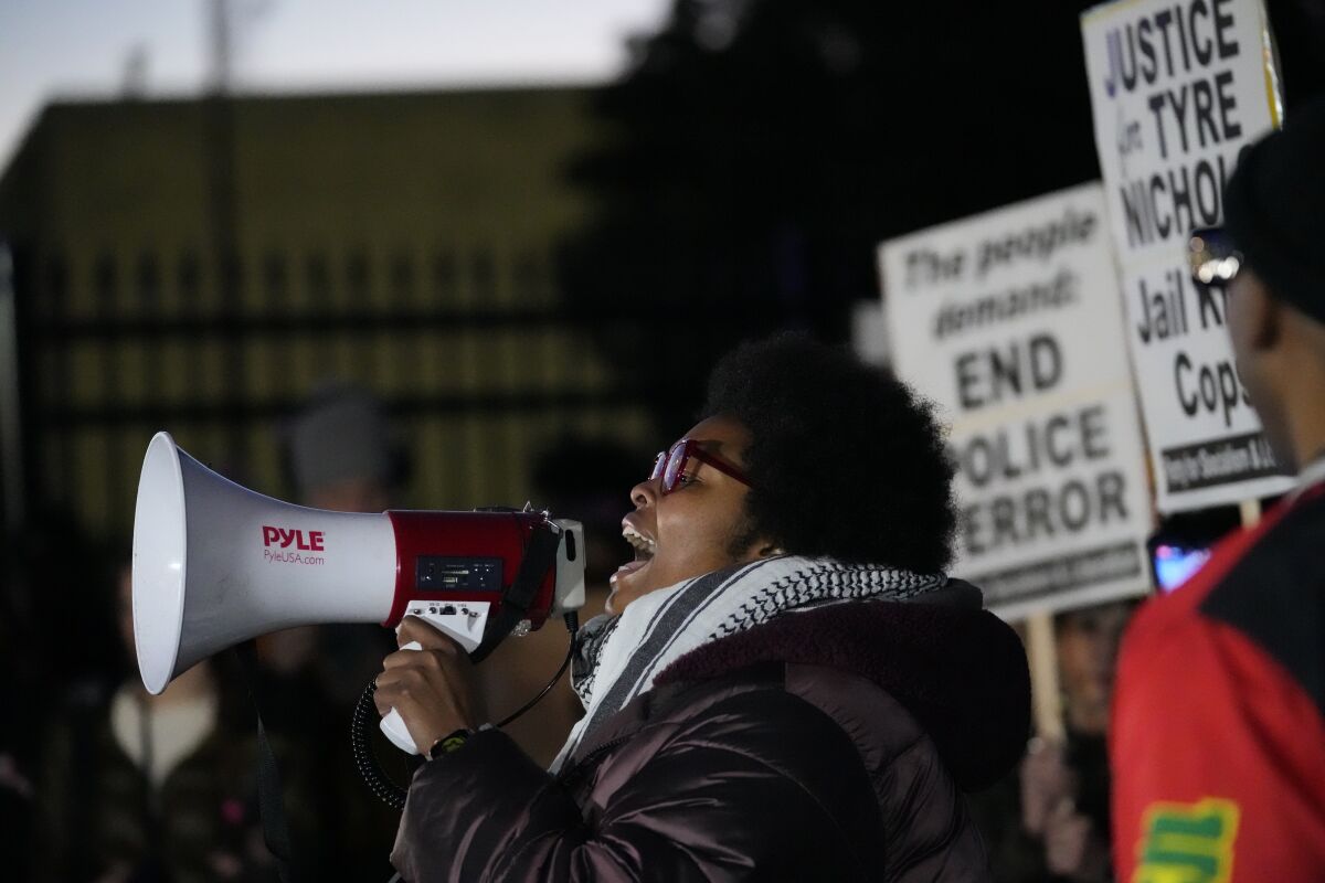 A woman speaking into a microphone as people hold signs