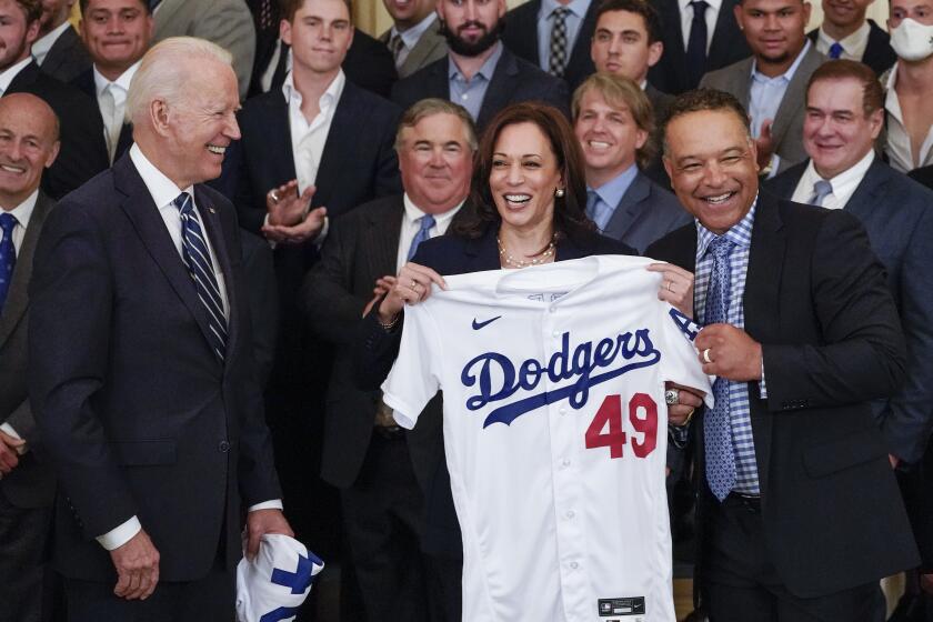 President Joe Biden, left, reacts as he watches Vice President Kamala Harris, center, pose with Los Angeles Dodgers.