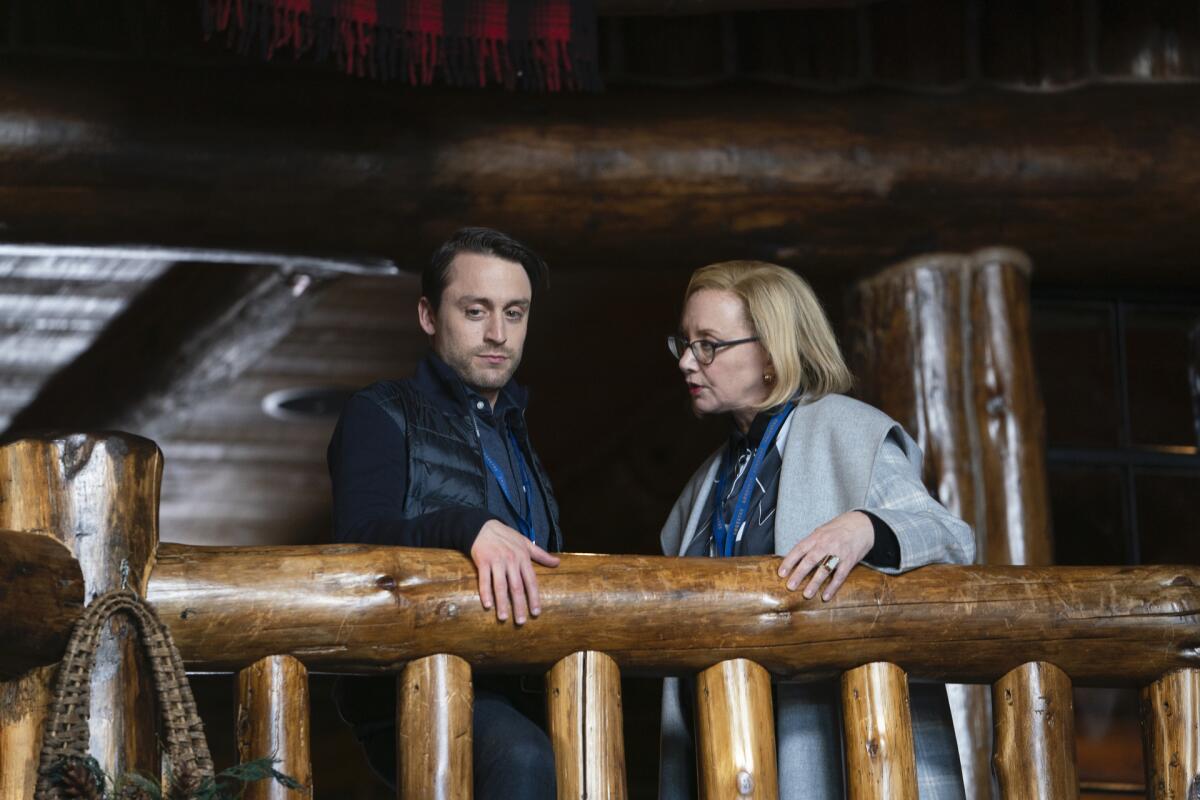 A young man and older woman in serious conversation on a rustic mezzanine with rough-hewn wood railings in "Succession."