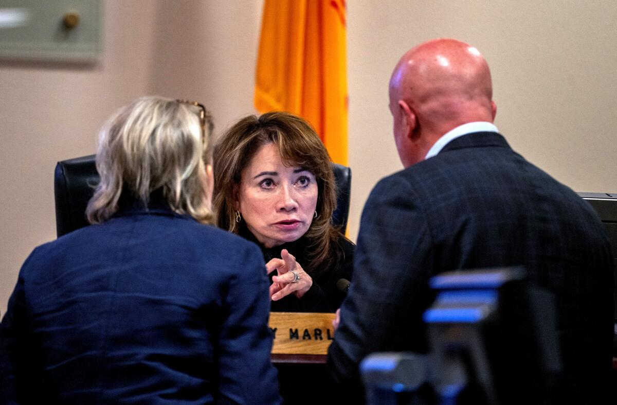 A judge leans forward to speak with a man and a woman with their backs to the camera