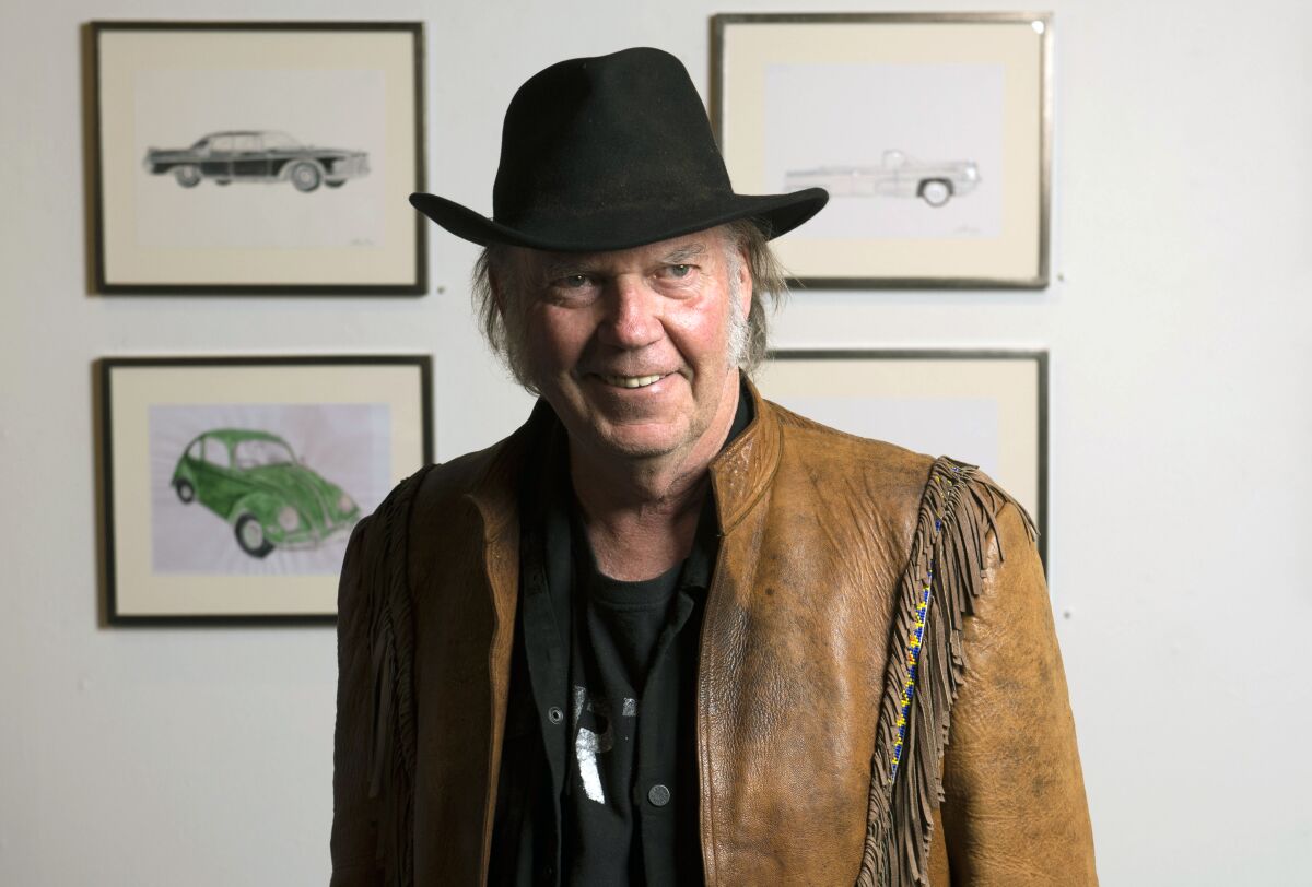 A man in a cowboy hat stands in front of four paintings in an art gallery.