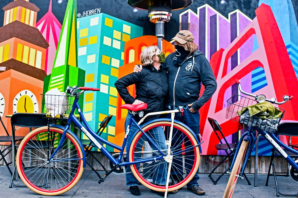 A couple with bikes in front of a cityscape mural