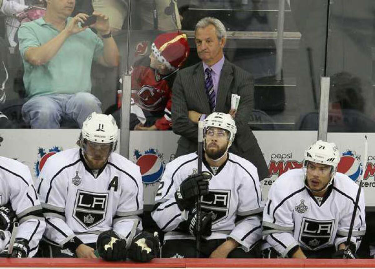 Darryl Sutter stands along the Kings bench (with a little Devil behind him) during Game 5 in New Jersey.