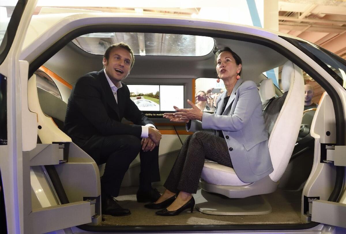 France's economy and industry minister Emmanuel Macron takes a seat in an 'autonomous' driverless electric car with ecology, sustainable development and energy minister Segolene Royal at the opening of the 2014 Paris auto show, which drew official emphasis on green tech behind the wheel.