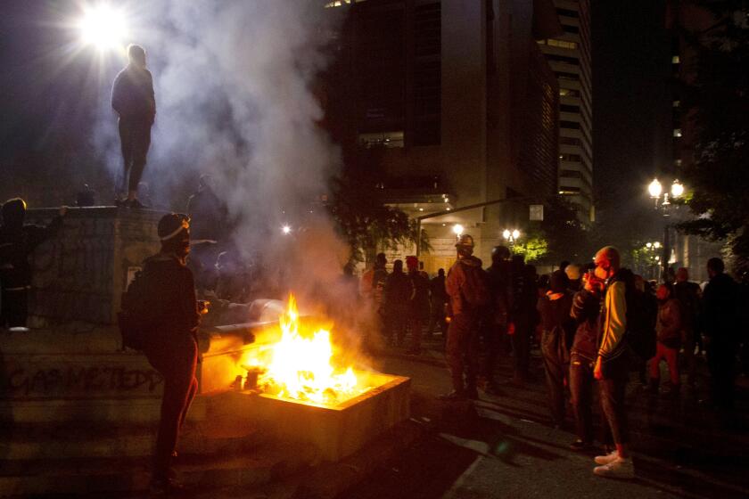 FILE - In this July 4, 2020, file photo, protesters gather near a fire in downtown Portland, Ore. Oregon's largest city is in crisis as violent protests have wracked downtown for weeks. The mayor can't bring the council along on cracking down because of very liberal council members and no matter what he does, the city gets sued anyway. Meanwhile, downtown businesses are being destroyed on top of the pandemic and the rank-and-file police are increasingly venting their frustration. (Beth Nakamura/The Oregonian via AP, File)