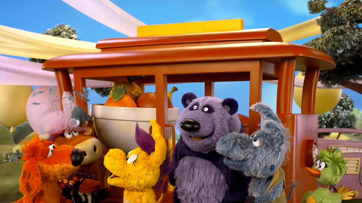 Dog, cow, donkeys, panda and duck puppets stand around a red trolley car.