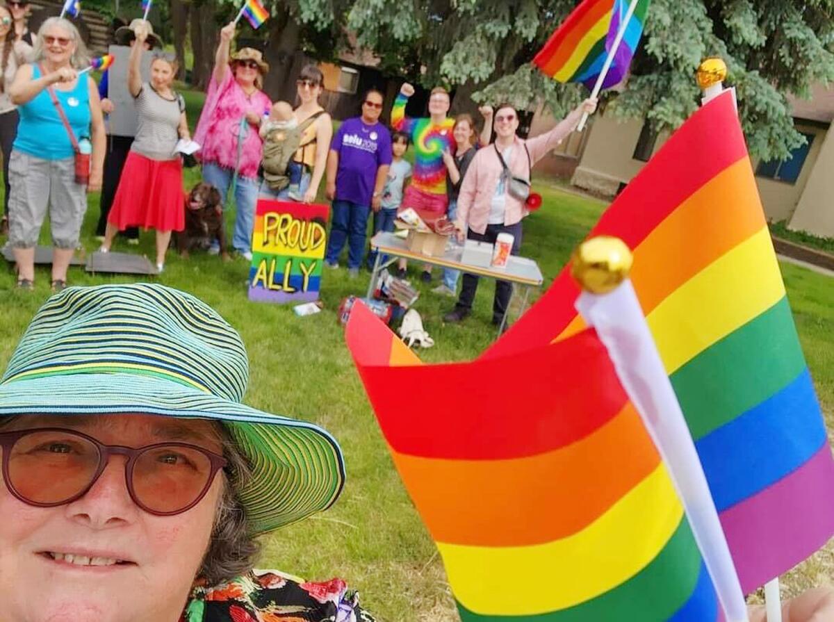 A person takes a selfie with a rainbow flag in front of a crowd